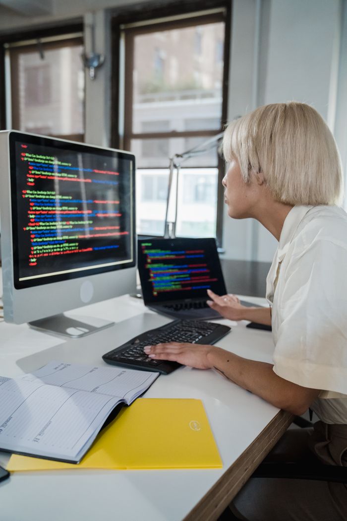 The Art of Drawing Readers In: Your attractive post title goes here Woman with blonde hair programming on a computer in a modern office, focused on multicolored script on screen.